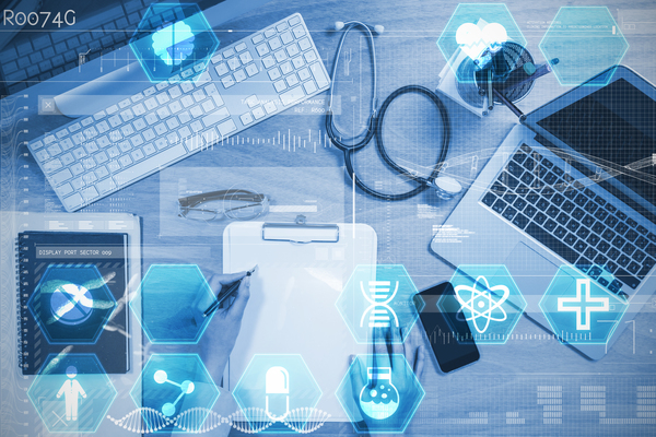 The image is a birds eye view of a data scientist's laptop, computer keyboard, a stethoscope, a clipboard and pen, a notebook & a smart phone spread across a desk. The image has a light blue filter over the top and various data science icons scattered around the edges.